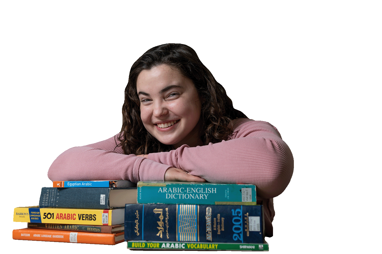A student rests her arms on a stack of books and smiles