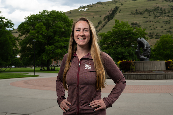 Anna smiles for a portrait wearing University of Montana apparel in front of the grizzly bear statue along the Oval on the University of Montana campus in Missoula, MT.
