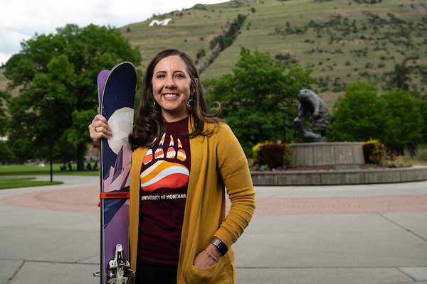 Julie Ann Williams stands her skis next to her and smiles for a portrait wearing University of Montana apparel in front of the grizzly bear statue along the Oval on the University of Montana campus in Missoula, MT.