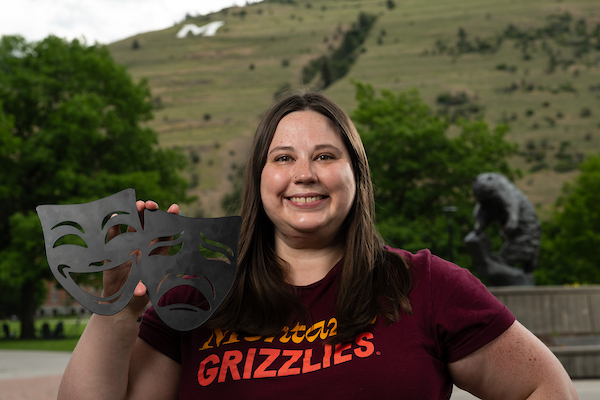 Sophia smiles for a portrait, wearing UM apparel in front of the grizzly bear statue along the Oval on the University of Montana campus in Missoula, MT.