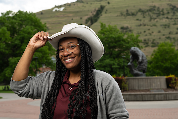Zen smiles for a portrait, wearing a cowboy hat and University of Montana apparel in front of the Grizzly bear statue along the Oval on the University of Montana campus in Missoula, MT.