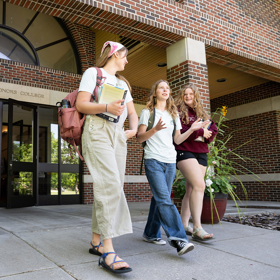 Three students talk as they exit the Davidson Honors College Building at UM