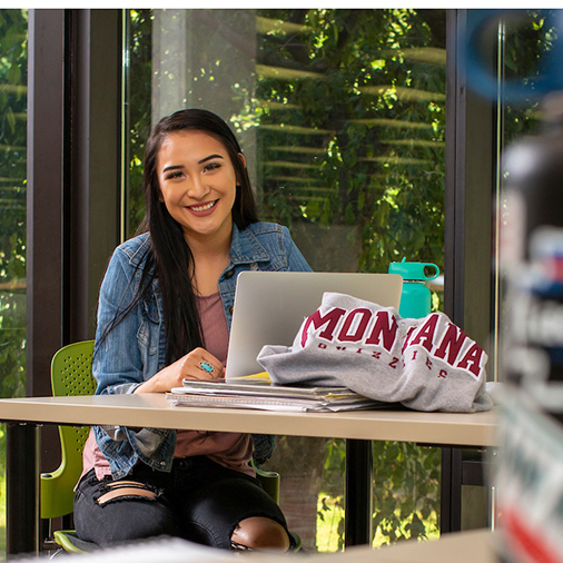 A student looks up from her laptop while studying in the Mansfield Library and smiles