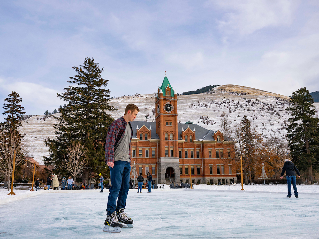 A student ice skates on the rink on the Oval. Main Hall stands in the background.