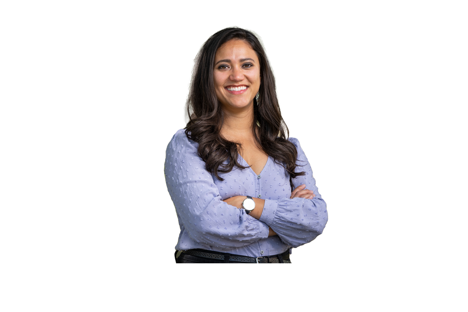 A University of Montana Department of Counseling master’s graduate student with long brunette hair, wearing a periwinkle colored blouse and a wristwatch stands smiling with arms crossed for a portrait outside of the Curry Health Center on the University of Montana campus